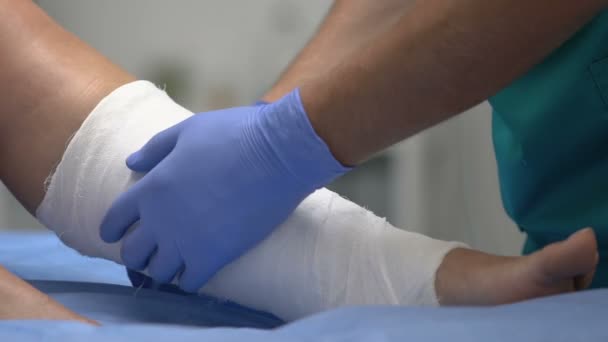 Médico poniendo vendaje de rodillos en la pierna del paciente, tratamiento médico en el hospital — Vídeo de stock