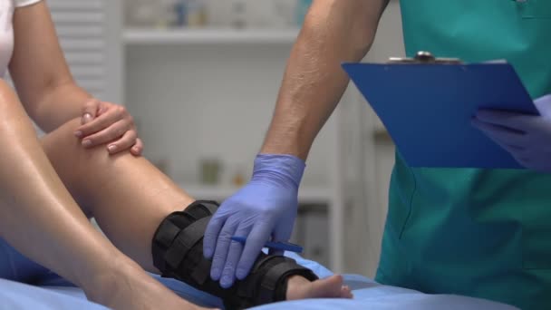 Läkare kontrollera patientens ben i fotled wrap, inspelning undersökningsresultat, hälsa — Stockvideo