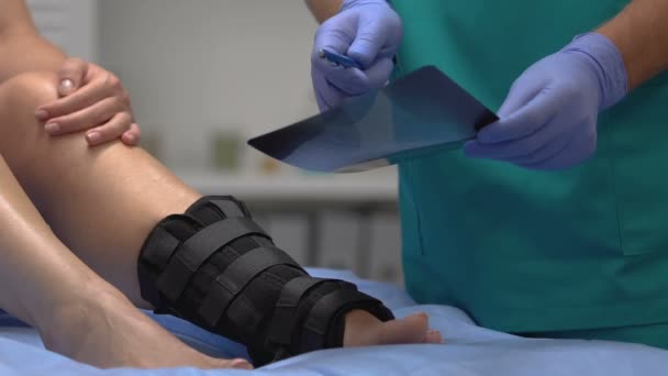 Traumatolog wyjaśniający wyniki rentgenowskie pacjentowi z okładem na kostkę, opieką zdrowotną — Wideo stockowe