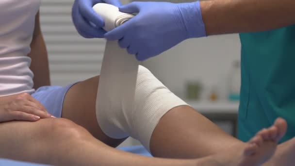 Врач снимает эластичную повязку с колена пациента, операция по замене суставов — стоковое видео