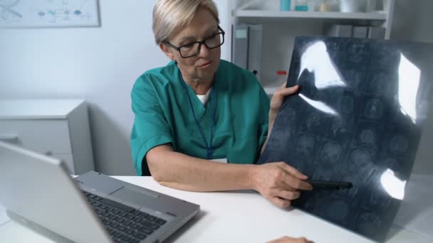 Невролог показывает и объясняет женщине МРТ мозга, пова пациента, советы — стоковое видео