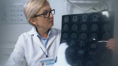 Hasta, elinde beyin röntgeni olan yetişkin kadın doktoru izliyor.