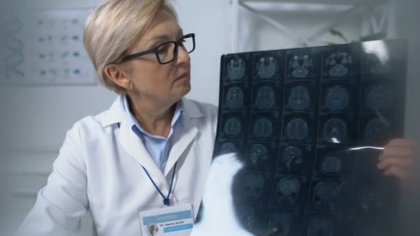 Пацієнт спостерігає за зрілою жінкою-лікаркою, яка проводить рентгенівський медичний огляд мозку — стокове відео