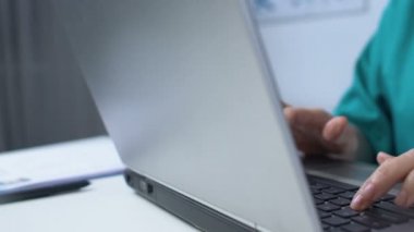 Dizüstü bilgisayarda yazan yaşlı bir tıp çalışanı, hasta verilerini çevrimiçi kayıtlara kaydediyor.