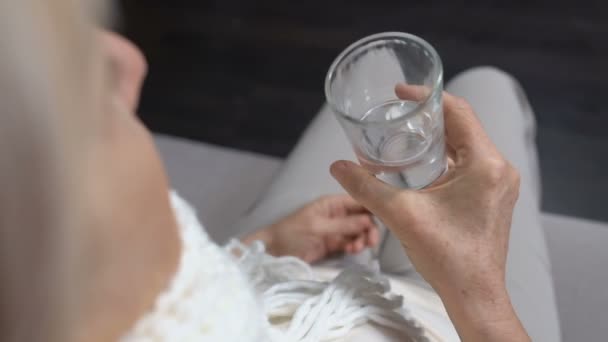 Mujer mayor en bufanda bebiendo agua en casa, tratamiento contra la gripe o el resfriado, atención médica — Vídeo de stock