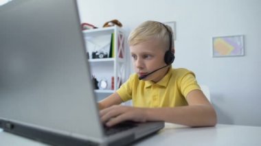 Anne masaya kitap koyuyor, oğul kulaklıkla bilgisayar bağımlılığı oyunu oynuyor.