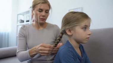 Bakıcı anne örgü örüyor ve güzel küçük kızının, ailesinin saçlarını tarıyor.
