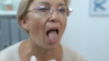 Erkek otolarolog yaşlı kadının boğazını kontrol ediyor, grip virüsü belirtileri.