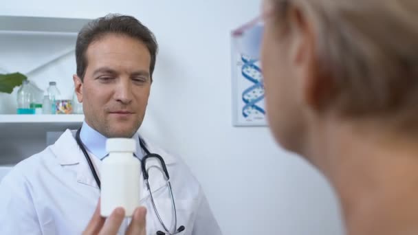 Врач-мужчина предлагает пациентке банку витаминов, медицинскую поддержку в старости — стоковое видео
