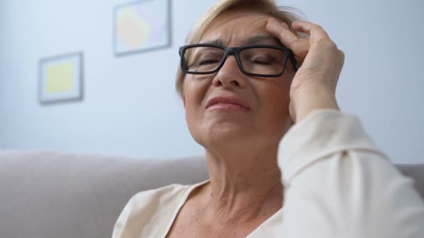 Пожилая женщина в очках страдает головной болью принимая таблетки от высокого давления — стоковое видео