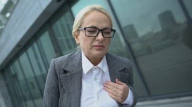 İş elbiseli kadın göğüs bölgesinde şiddetli ağrı ve kalp krizi belirtileri gösteriyor.