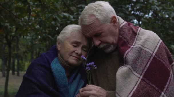 Pareja anciana molesta envuelta en cuadros abrazando la celebración de la flor en las manos, el dolor — Vídeos de Stock