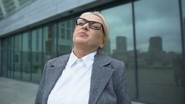 Зрелая женщина-босс в очках поворачивает голову, страдает от боли в шее на открытом воздухе, боли — стоковое видео