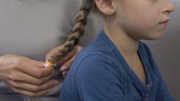 Mãe jovem trançando cabelo de filha pequeno, preparação antes da escola, close-up — Vídeo de Stock