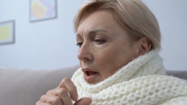 Starzejąca się kobieta w szaliku kaszle i przyjmuje tabletki w domu, grypę lub leczenie przeziębienia — Wideo stockowe