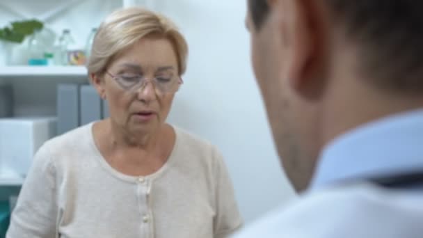 Elderly female patient massaging temples, complaining doctor on migraine pain — Stock Video