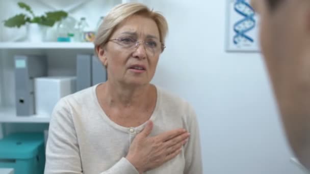 Зрелая пациентка держит руку на груди, жалуется доктору на боль в сердце — стоковое видео