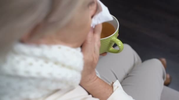 Seniorin niest in Gewebe und trinkt zu Hause heißen Tee, Grippeepidemie