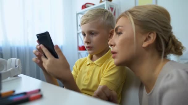 Menino bonito mostrando mãe novo aplicativo smartphone, tecnologias modernas, gadgets — Vídeo de Stock