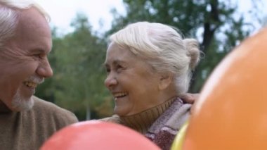 Neşeli olgun çift ellerinde balonlarla gülümsüyor, yıldönümü kutlaması yapıyorlar.