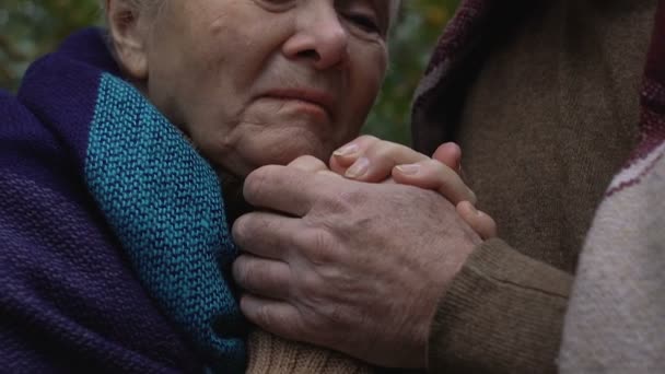 Стара жінка плаче, тримаючись за руки чоловіка, соціальна незахищеність пенсіонерів — стокове відео