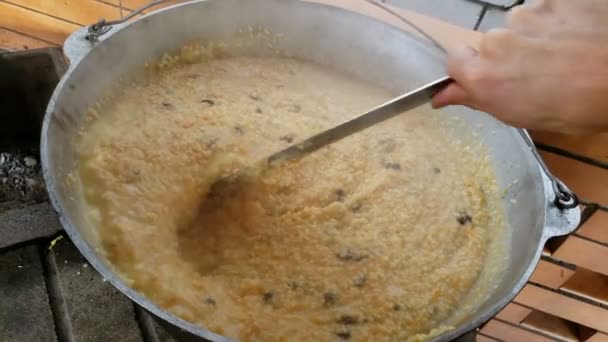 Koch rührt traditionellen Brei durch Schöpfkelle in riesigen Topf und bereitet Wohltätigkeitsessen zu — Stockvideo