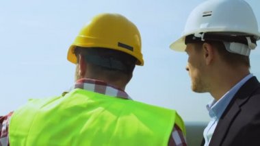 Kasklı müteahhit ve erkek müşteri çatıdaki inşaatı tartışıyorlar.