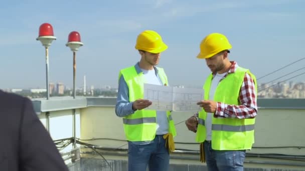 Ingeniero varón feliz en casco sonriendo en la leva, constructores discutiendo esquema de la casa — Vídeos de Stock