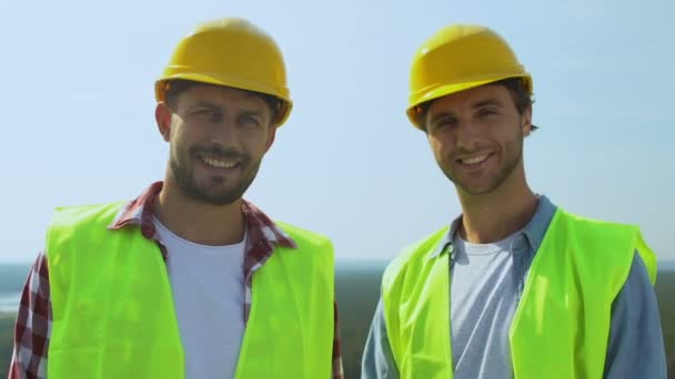 Constructores masculinos experimentados en cascos y uniforme sonriendo en cámara, buen servicio — Vídeos de Stock
