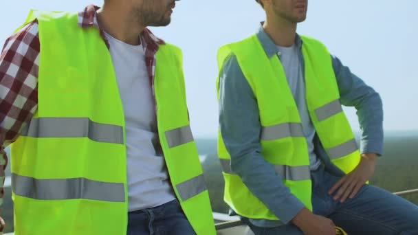 Ontspannen bouwers in uniform praten op het dak tijdens de werkvakantie, beroep, rust — Stockvideo