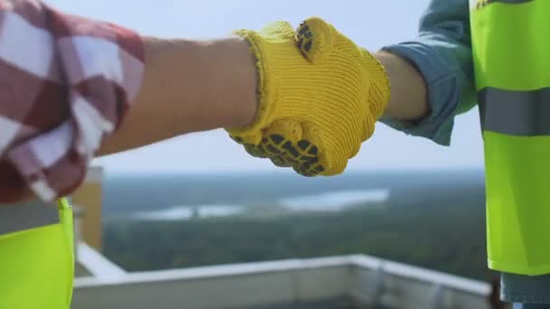 Bauunternehmer und Bauunternehmer in Uniform geben sich auf dem Dach die Hand, arbeiten zusammen, verhandeln — Stockvideo