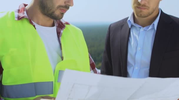 Biznesmen omawiający plan budowy z wykonawcą w mundurze na dachu — Wideo stockowe