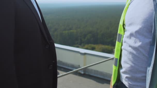 Zakenman schudt hand bouwer in uniform op dak, succesvolle samenwerking — Stockvideo