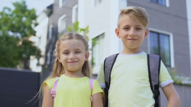 Broer knuffelen kleine zus, kijken naar de camera en glimlachen eerste dag op school — Stockvideo