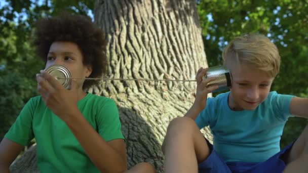 Amigos multirraciales hablando a través de latas sentadas en el parque, infancia feliz, diversión — Vídeos de Stock