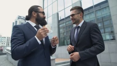 Takım elbiseli bir adam midesinde ağrı hissediyor ve dışarıda sandviç yiyor.