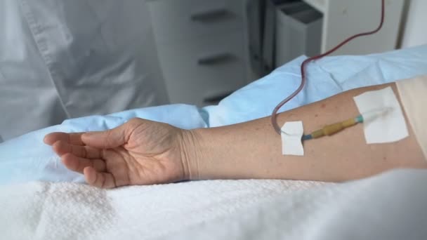 Врач беспокоится о тяжелобольном пациенте, держащем ее за руку во время процедуры — стоковое видео