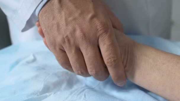 Man dokter zet bewusteloze vrouw patiënt hand op bed, hard beroep — Stockvideo