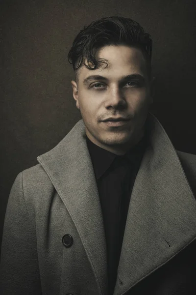 Vintage and retro portrait of illuminated  man in grey coat with brown background. Young guy with old hairstyle. Fashion portrait of man (Vintage). Male model shot in studio on dark (black) background