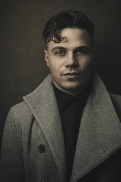 Vintage ve retro kahverengi zemin ile gri paltolu ışıklı adam portresi. Eski saç modeli ile genç bir adam. Adam (Vintage) moda portre. Erkek modeli Studio koyu (siyah) arka planda vurdu
