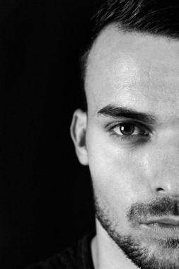 Güzel genç adam koyu siyah arka plan üzerinde koyu renk güzel gözleri ile siyah beyaz portre. Yarım yüz portre sakal ve yüzünün keskin hatları olan adam. Çekici adam yarım yüz kapatmak yukarıya fotoğraf.