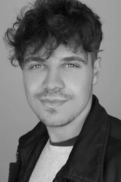 Siyah ve beyaz moda portre fotoğraf genç ve yakışıklı adam kıvırcık saç ve deri ceket. Siyah ve beyaz adam sevimli gülümseme ile erkek portresi. Kamera için güzel çekici adam possing