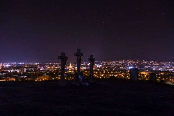 Ночь города в Нитре с смотровой площадки на вершине холма (горы) словацкого города Нитра с фиолетовым ночным небом и крестами. Центр города ночью со зданиями и церквями. Город ночью со звездами — стоковое фото