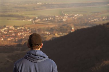 Kayanın üzerinde duran ve arka plan üzerinde bulanık Köyü ile manzarayı yetişkin adam (fiyatı). Gün batımında ormandaki turist adam silüeti.