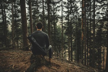 Genç adam (camper ve uzun yürüyüşe çıkan kimse) güdük'in iğne yapraklı orman üzerinde oturan ve muhteşem manzarayı. Ormanda tek başına - adam. Dinlenme ve ormanda rahatlatıcı.