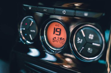 Kadının elleri arabanın havalandırma sistemini çeviriyor. Gösterge panelinde yeni arabadaki soğuk hava için düğme var. Turuncu panel. Klima düğmeli ve Celsius dereceli iklim kontrol görüntüsü - 19.