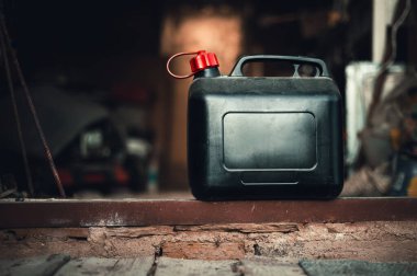 Old and dirty plastic black gas can  fuel container standing on ground from bricks with garage on background. Black petrol can with a lot of tools in storage (workshop). 