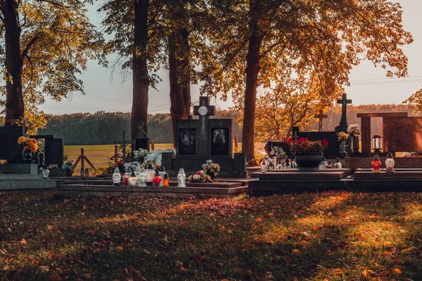Illuminated Tombstones at a Christian cemetery in fall.Time before All Saints Day. Photo of colorful cemetery with gravestones, flowers with sunset on background.