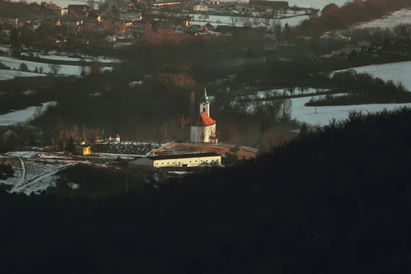 Vue depuis les collines sur un paysage gelé d'hiver avec église chrétienne et cimetière au milieu - couvert de neige. Photo de dessus les collines de la vallée avec village et vieille église - coucher de soleil . — Photo