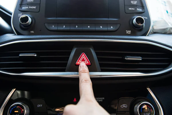 Dedo presionando un botón de luces de advertencia de peligro en un coche coreano de lujo moderno Imagen De Stock